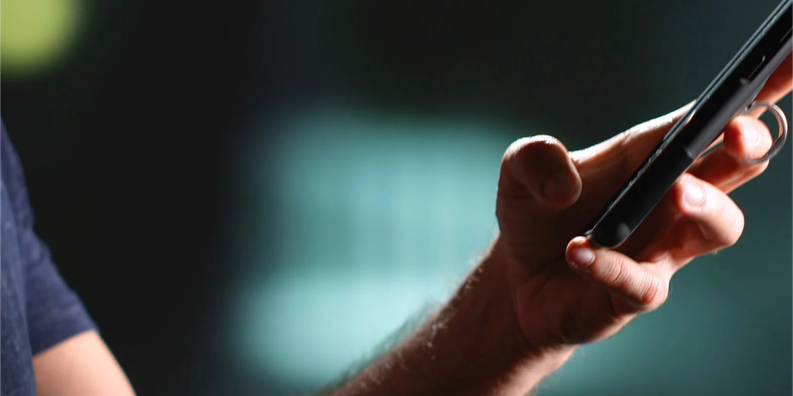 Una mano sostiene un teléfono de perfil sobre un fondo verde oscuro desenfocado